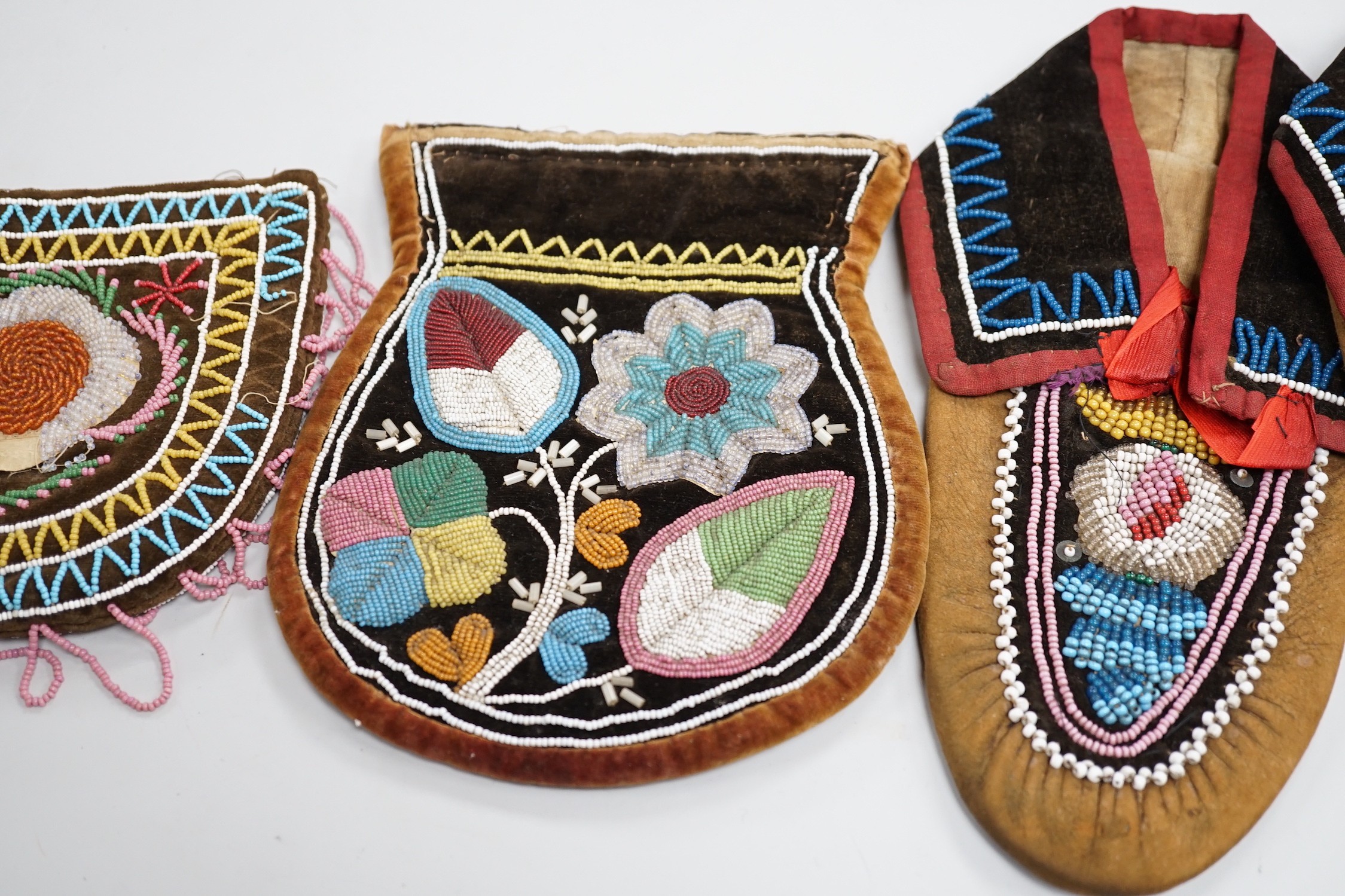 A pair of mid to late 19th century Mikmaq, North American Indian, moccasins, worked in floral beadwork on vamp, with velvet cuffs and red silk ties, together with two Wabanaki floral bead-worked velvet bags